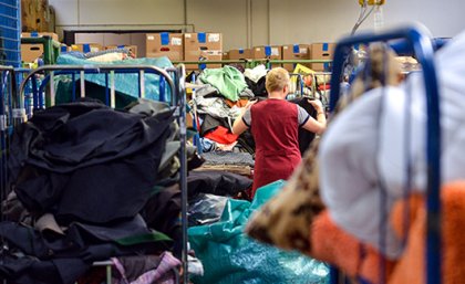 A woman sorting through piles of clothes at a charity shop